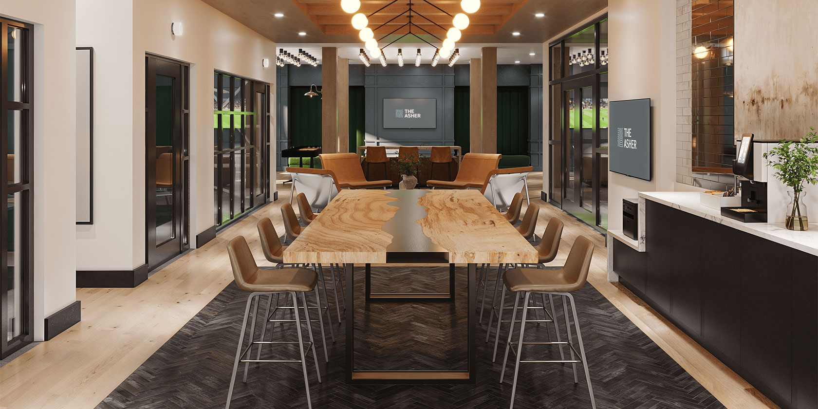 Co-working and lounge space at The Asher featuring a long wood-and-black table with modern barstool seating, dramatic globe lighting suspended from exposed wood beams, and large wall-mounted TVs displaying The Asher logo. The space includes a built-in coffee station, a comfortable seating area, and glass doors leading to additional amenity rooms.